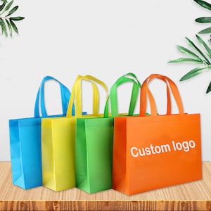 May include: Four colorful tote bags in blue, yellow, green, and orange, each with matching handles. The orange bag has the text "Custom logo" in white. The bags are made of a non-woven material and are suitable for shopping or promotional use.
