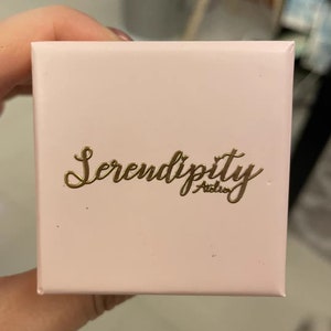 May include: A pink box with the words "Serendipity Atelier" in gold lettering.