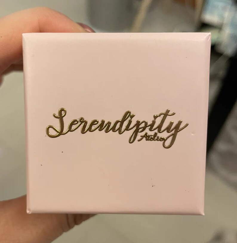 May include: A pink box with the words "Serendipity Atelier" in gold lettering.