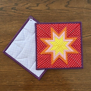 May include: A red, yellow, orange, and pink star-shaped pot holder with white polka dots on a white background. The pot holder has a purple border.