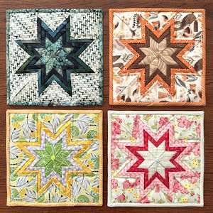 May include: Four square quilted coasters with star designs. Each coaster features a different color scheme: teal and green, orange and brown, yellow and green, and pink and red. The coasters are made of fabric and have a stitched border.
