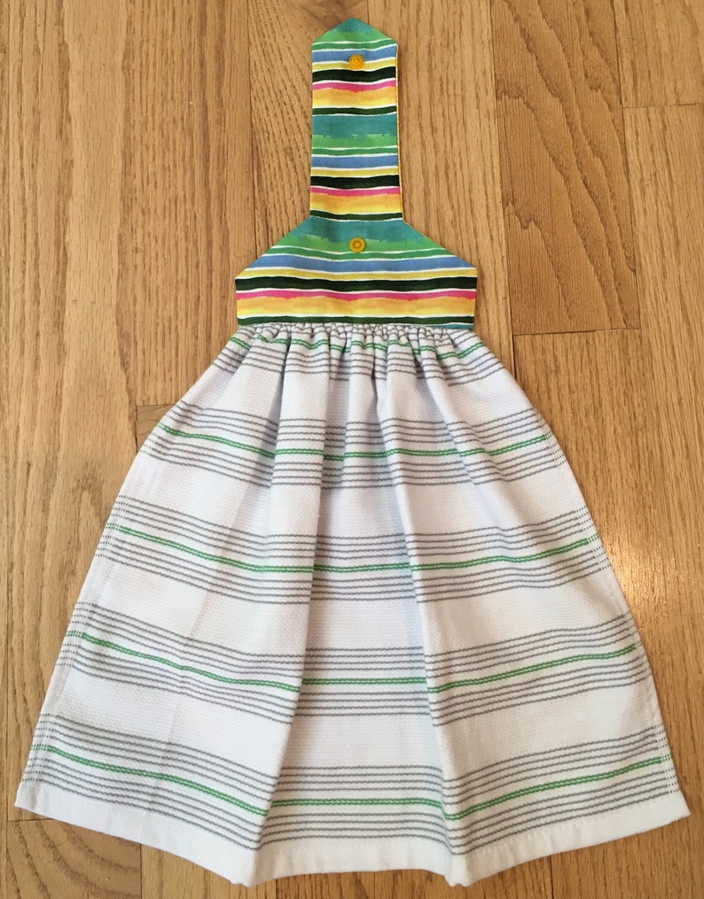 May include: A white kitchen towel with green and gray stripes. The towel has a colorful striped hanging loop with yellow buttons.