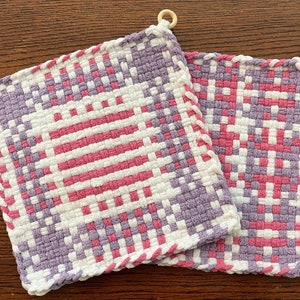 May include: Two purple, pink, and white woven pot holders with wooden rings.