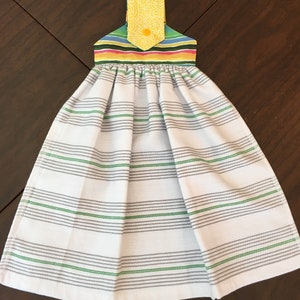 May include: A white kitchen towel with gray and green stripes. The towel has a colorful striped hanging loop with a yellow floral pattern.