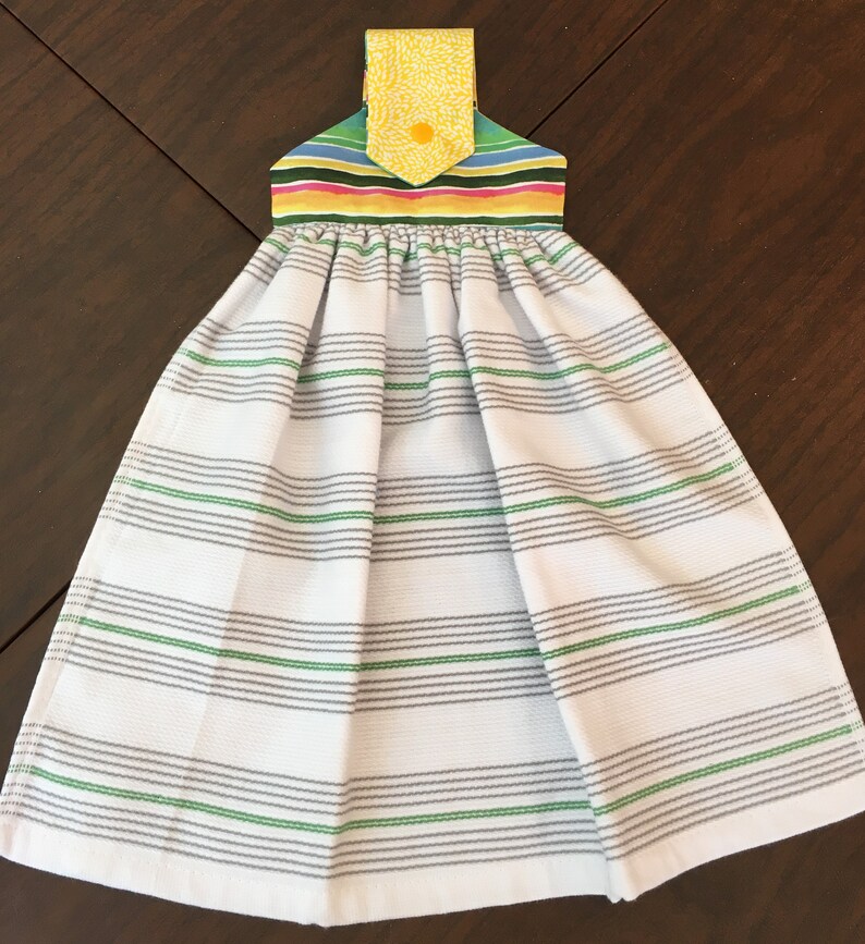 May include: A white kitchen towel with gray and green stripes. The towel has a colorful striped hanging loop with a yellow floral pattern.