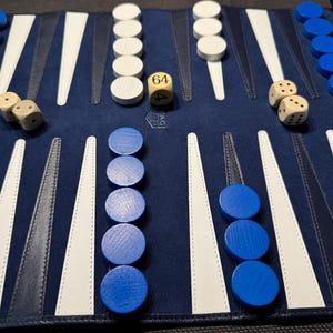 May include: A backgammon board with blue and white triangles, blue and white game pieces, and dice. The board is open, showing the playing surface with pieces arranged for a game. The dice show the numbers 6 and 4.