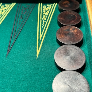Può includere: Un set da gioco di backgammon con un piano di gioco in feltro verde e sei pedine marroni scure.