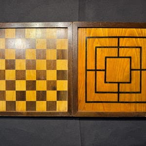 May include: A rectangular wooden game board featuring two distinct playing surfaces. The left side displays a classic eight-by-eight checkered grid in alternating light and dark wood tones, while the right side shows a nine-men's morris grid.