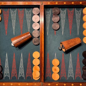 Può includere: Un set di backgammon con cornice in legno e superficie di gioco verde acqua. Il set include pedine in legno in colori chiari e scuri, dadi e coppette per dadi in pelle. Il tabellone è aperto, pronto per giocare.