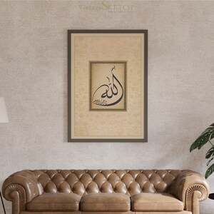 Pu&ograve; includere: Una stampa incorniciata con uno sfondo beige e un design di calligrafia nera della parola "Allah" in una cornice dorata. La stampa &egrave; appesa a un muro con un divano in pelle marrone e una pianta in vaso in primo piano.