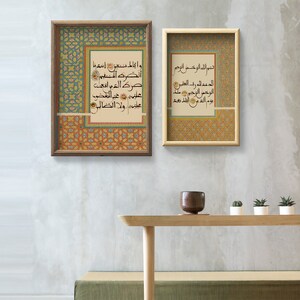 K&ouml;nnte beinhalten: Zwei gerahmte Drucke mit islamischer Kalligraphie in arabischer Schrift. Die Drucke sind vor einer hellgrauen Wand mit einem Holztisch und Topfpflanzen im Vordergrund platziert.