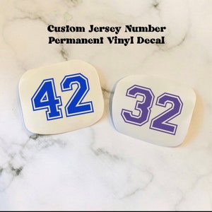 May include: Two custom jersey numbers, one blue 42 and one purple 32, on white backgrounds.  The numbers are outlined in white and have a vintage collegiate style font.  Custom Jersey Number Permanent Vinyl Decal.