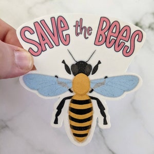 May include: A white sticker with the text "Save the Bees" in pink lettering. A cartoon bee with black, yellow, and blue coloring is centered on the sticker.