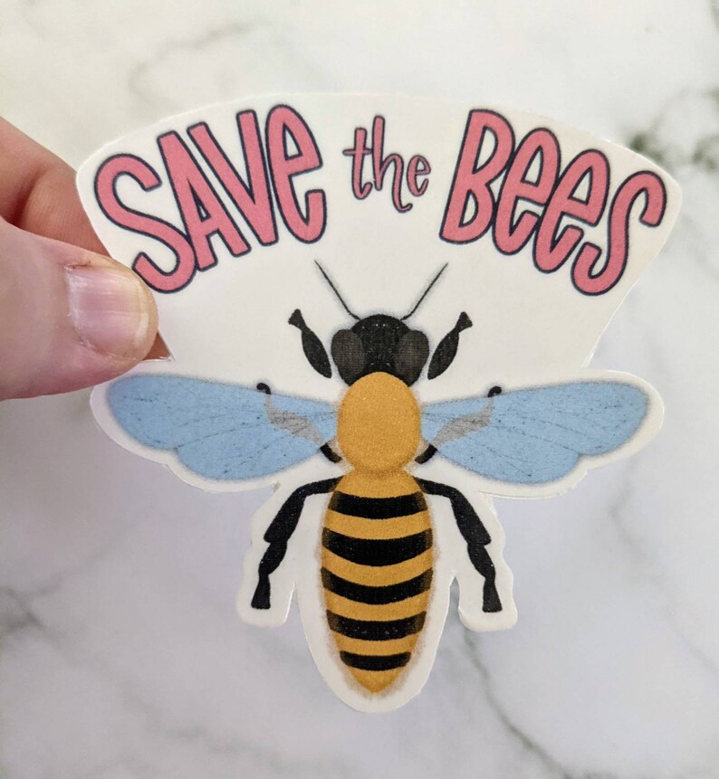 May include: A white sticker with the text "Save the Bees" in pink lettering. A cartoon bee with black, yellow, and blue coloring is centered on the sticker.