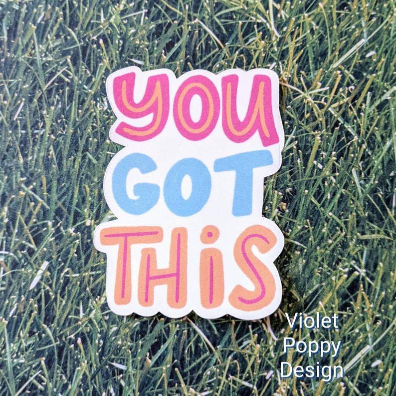 May include: A white sticker with the text "You Got This" in pink, orange, and blue lettering. The sticker is on a green grassy background.