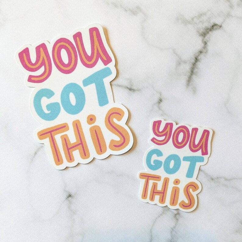 May include: Two stickers with the phrase "You Got This" in pink, blue, and orange lettering on a white background.