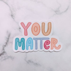 May include: A colorful sticker with the words "YOU MATTER" in a rainbow of colors. The letters are outlined in white and have a stitched effect.