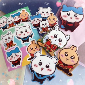 May include: A selection of colourful cartoon stickers featuring adorable bear and bunny characters. The stickers have blue, red, and orange accents. Some stickers are on a green and pink background. The stickers are in various poses.