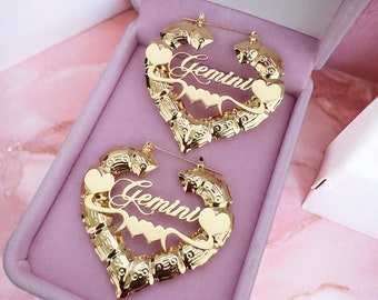 May include: Gold heart-shaped hoop earrings with the word "Gemini" inscribed on each earring. The earrings are displayed in a pink velvet box.