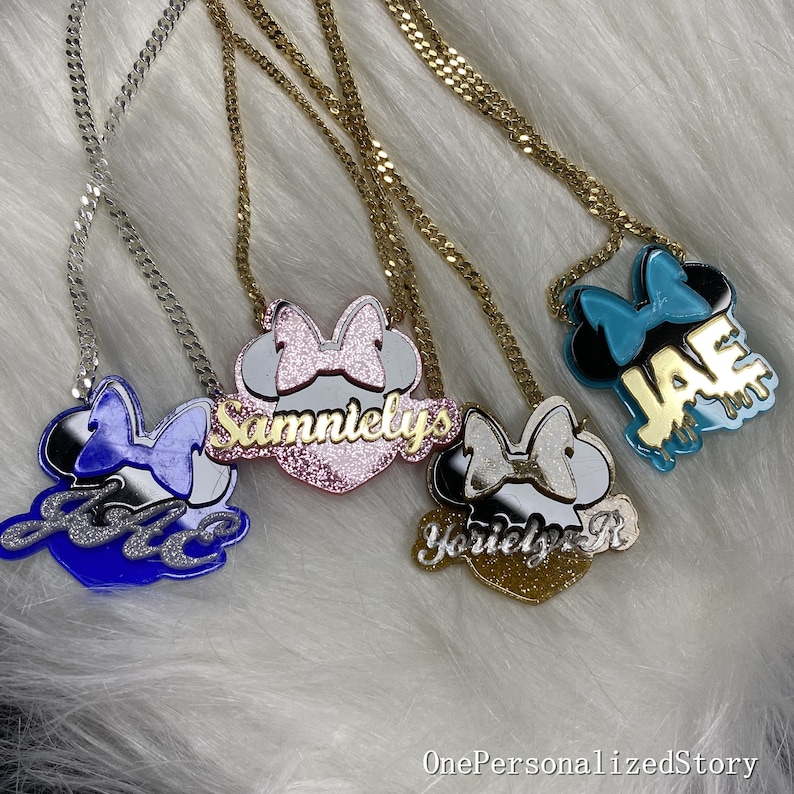 Op de afbeelding: Vier gepersonaliseerde kettingen met gouden kettingen en een Mickey Mouse-kopbedel met een strik. De bedels zijn versierd met glitter en de namen "Jada", "Sammielys", "Yorielys R" en "JAE" zijn in gouden letters geschreven.