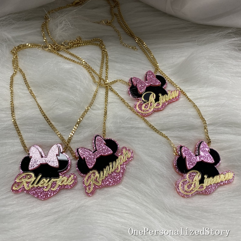 Op de afbeelding: Vier gouden kettingen met roze en zwarte Minnie Mouse-kopcharms. Elke charm heeft een andere naam: Riley Jo, Runyan, Jimia en Jimena.