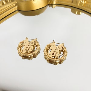 K&ouml;nnte beinhalten: Ein Paar goldfarbene Ohrringe mit einem Minnie Mouse-Silhouetten-Design und einem Bambus-inspirierten Rahmen.