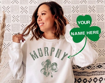 May include: White sweatshirt with a green shamrock and the word "MURPHY" in a distressed font. The text "YOUR NAME HERE" is written on a green shamrock in the top right corner of the image.