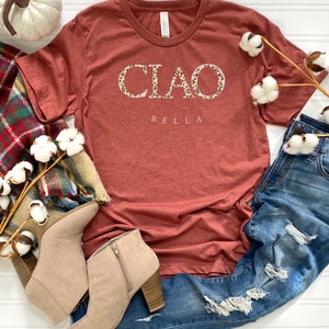 Puede incluir: Una camiseta de color &oacute;xido con la palabra "CIAO" en letras blancas con un estampado de leopardo. La palabra "BELLA" est&aacute; escrita en letras blancas debajo de la palabra "CIAO".