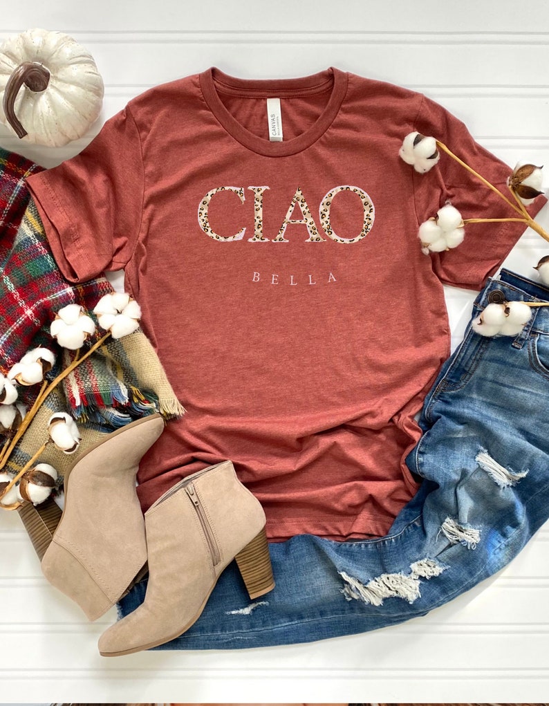 Puede incluir: Una camiseta de color &oacute;xido con la palabra "CIAO" en letras blancas con un estampado de leopardo. La palabra "BELLA" est&aacute; escrita en letras blancas debajo de la palabra "CIAO".