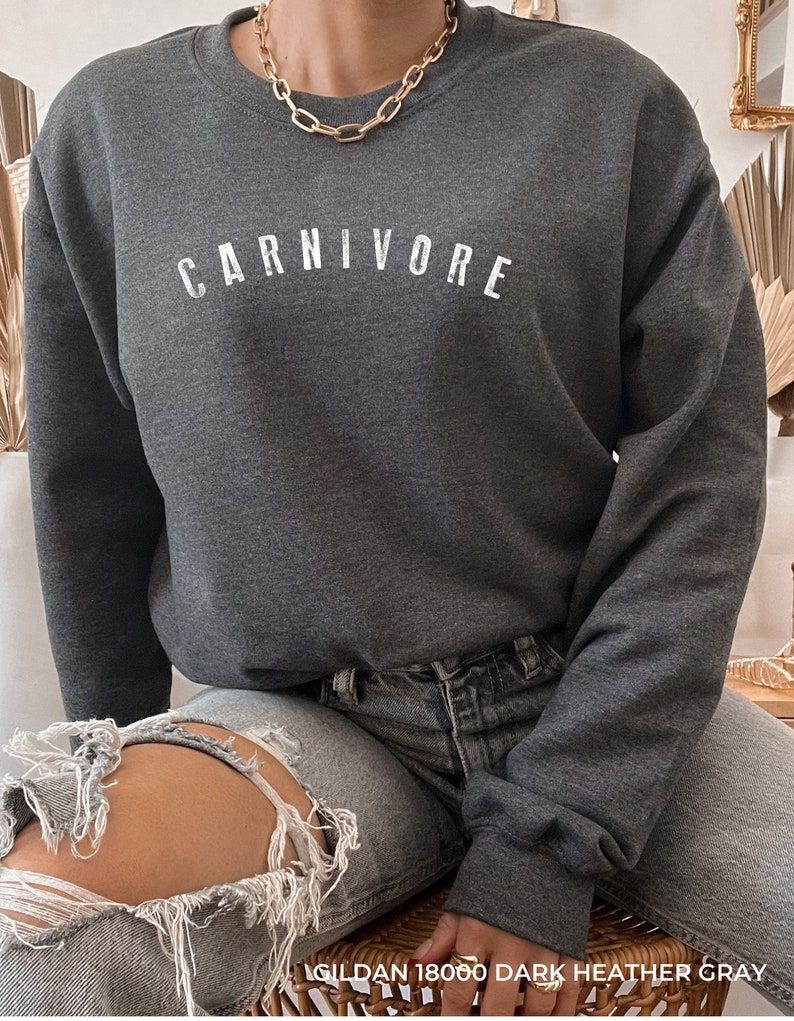 May include: A dark heather gray sweatshirt with the word "CARNIVORE" printed in white on the front. The sweatshirt is made by Gildan and is a size 18000.