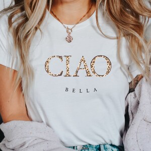 Puede incluir: Camiseta blanca con el texto "CIAO BELLA" en estampado de leopardo.