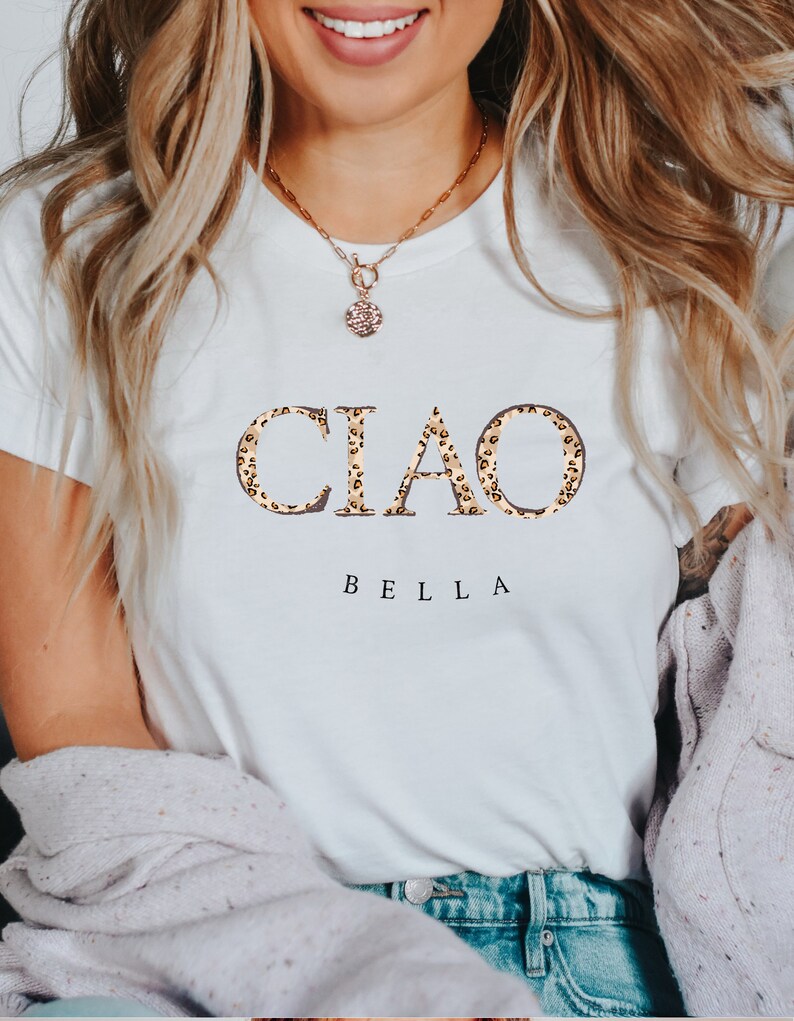 Puede incluir: Camiseta blanca con el texto "CIAO BELLA" en estampado de leopardo.
