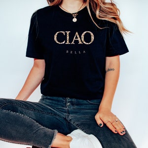 Puede incluir: Una camiseta negra con las palabras "CIAO BELLA" en letras doradas de purpurina.