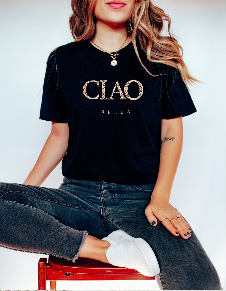 Puede incluir: Una camiseta negra con las palabras "CIAO BELLA" en letras doradas de purpurina.