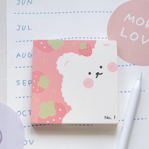 May include: A pink and white sticky note featuring a cartoon bear and strawberries. The note reads "No. 1" in the bottom right corner.