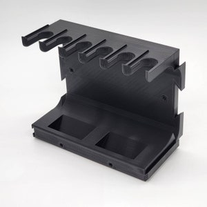 May include: Black plastic wall-mounted organizer with six slots for holding paintbrushes or other tools. The organizer has two compartments on the bottom.