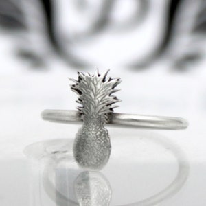 Könnte beinhalten: Ein silberner Ring mit einem Ananas-Design. Die Ananas ist detailliert und hat eine strukturierte Oberfläche.