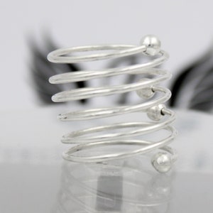 May include: Silver spiral ring with multiple coils and small beads. The ring is made of metal and has a shiny finish.
