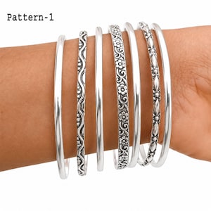 May include: A set of seven silver-toned bangles featuring various designs, including smooth polished bands, a wavy line pattern with dots, a floral motif, and a textured geometric pattern. The text Pattern-1 is visible in the upper left corner.