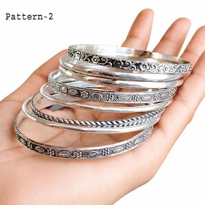 Close-up of stacked 925 sterling silver bangles on a wrist, highlighting the different handcrafted patterns and polished silver finish.