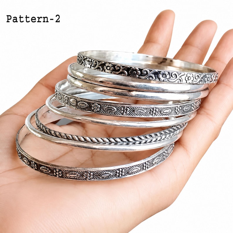 Close-up of stacked 925 sterling silver bangles on a wrist, highlighting the different handcrafted patterns and polished silver finish.