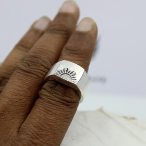 May include: A silver ring with a sun design on the top. The ring is worn on a person's finger.