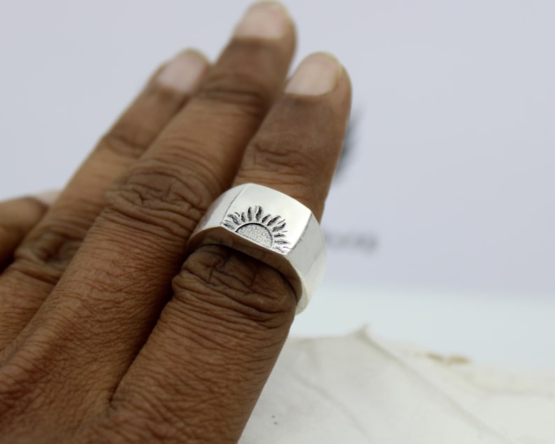 May include: A silver ring with a sun design on the top. The ring is worn on a person's finger.