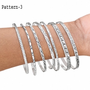 Multiple sterling silver bangles displayed together on a hand, showing the closed round shape and variety of decorative textures.