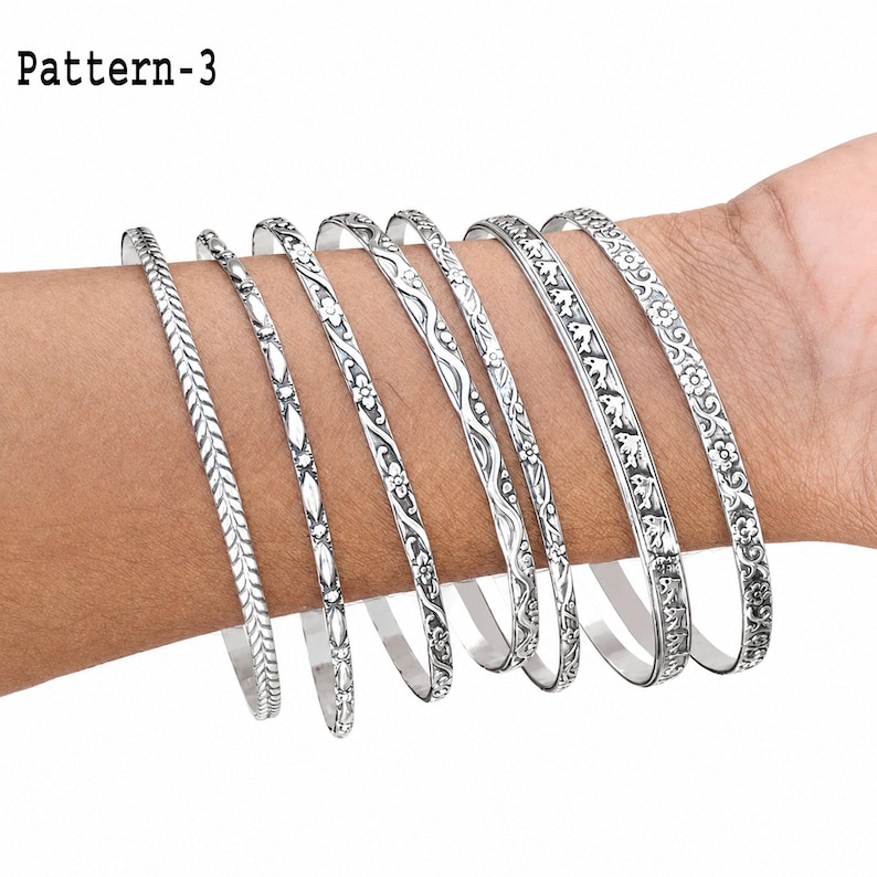 Multiple sterling silver bangles displayed together on a hand, showing the closed round shape and variety of decorative textures.