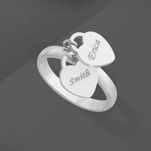 May include: Silver ring with two dangling heart charms. The charms are engraved with the names "Erica" and "Smith".