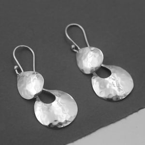 May include: A pair of silver dangle earrings with a hammered texture. Each earring features two teardrop-shaped pieces.