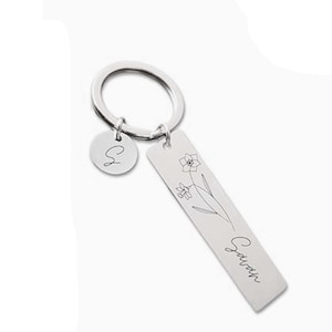 Puede incluir: Llavero plateado con un dije redondo con la letra "S" y una etiqueta rectangular. La etiqueta presenta un diseño floral y el nombre "Sarah". Un accesorio personalizado.