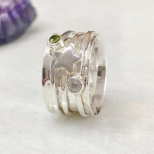 May include: A silver spinning ring with a star charm, a green gemstone, and a clear gemstone. The ring is made of multiple bands that spin around each other.