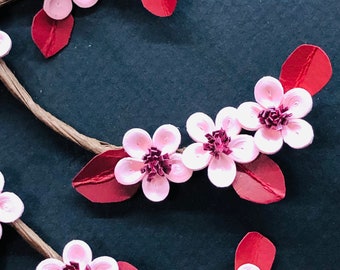 Peut inclure: Gros plan d'une branche de fleurs de cerisier en papier quilling avec des fleurs roses, des feuilles bordeaux et une tige brune sur fond sombre. Les fleurs ont un centre rose foncé. L'art du papier est un artisanat décoratif.